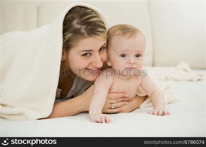 Toned portrait of happy young mother lying with her baby son under blanket