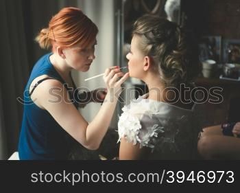 Toned portrait of makeup artist preparing blonde bride at morning