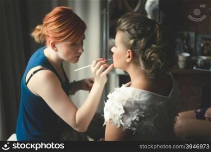 Toned portrait of makeup artist preparing blonde bride at morning