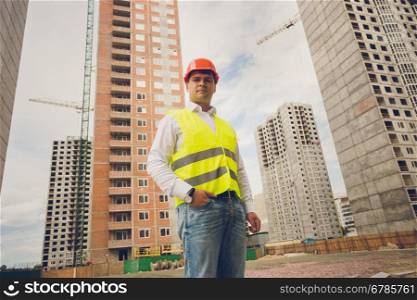 Toned portrait of smiling engineer posing against buildings under construction