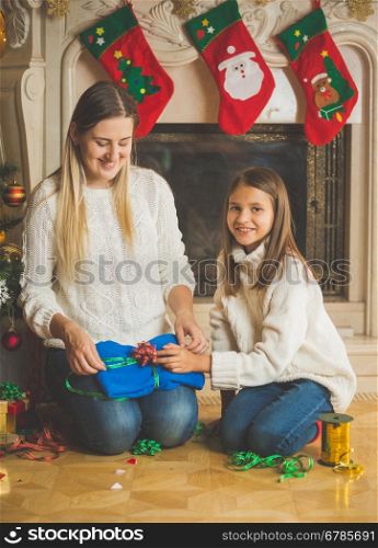 Toned portrait of smiling girl with her mother packing pullover in paper and gift box for Christmas