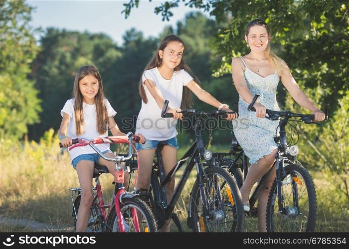 Toned portrait of two sister cycling with mother at meadow by the lake