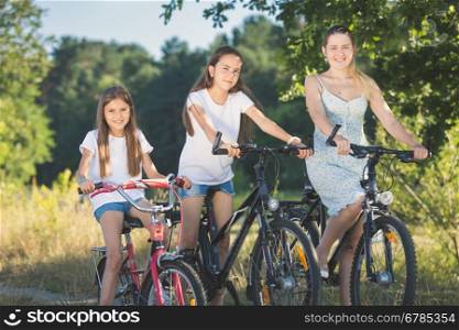 Toned portrait of two sister cycling with mother at meadow by the lake