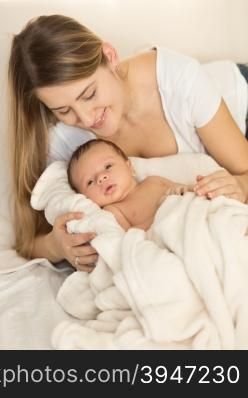 Toned portrait of young caring mother hugging newborn baby on bed