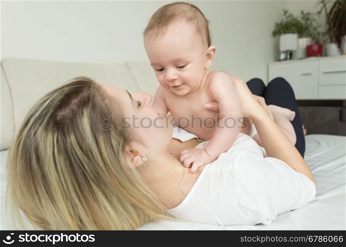 Toned portrait of young happy mother lying on bed and holding her baby
