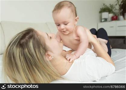 Toned portrait of young happy mother lying on bed and holding her baby