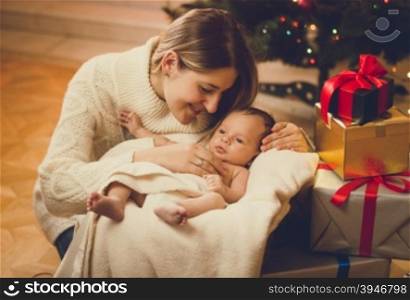 Toned portrait of young mother kissing baby boy lying in living room decorated for Christmas