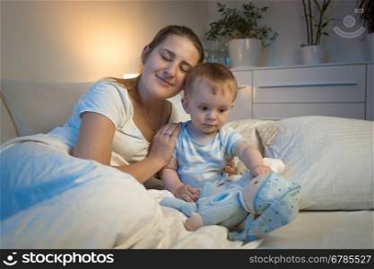 Toned portrait of young mother lying in bed with her baby boy at night