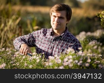 Toned portrait of young smiling man pruning flowers at garden