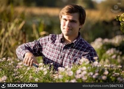 Toned portrait of young smiling man pruning flowers at garden