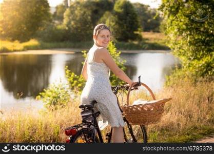 Toned portrait of young woman in dress sitting on bike at the lake