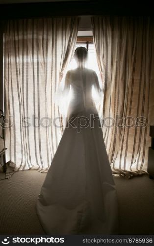 Toned shot of elegant bride looking out window at hotel room