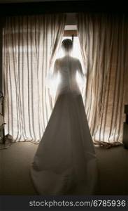 Toned shot of elegant bride looking out window at hotel room