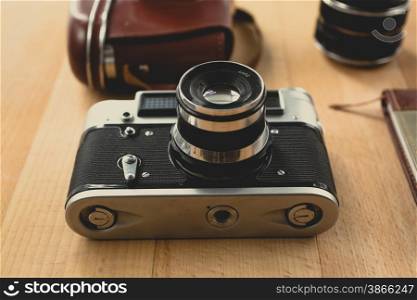 Toned shot of retro manual camera with portrait lens lying on wooden desk