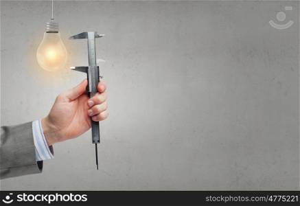 Tool in hand. Close up of hand measuring light bulb with wrench