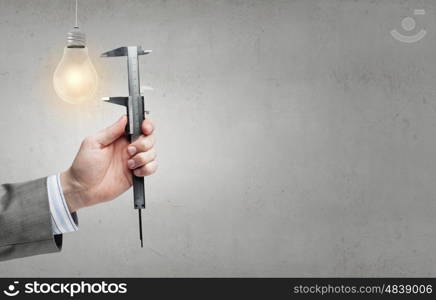 Tool in hand. Close up of hand measuring light bulb with wrench