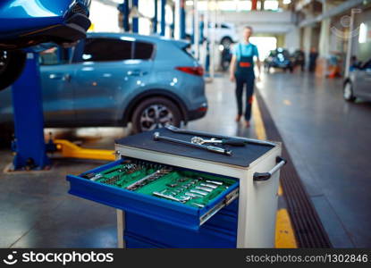 Toolbox, worker stands at vehicles on lifts on background, car service station. Automobile checking and inspection, professional diagnostics and repair. Toolbox, worker at vehicles on lifts on background