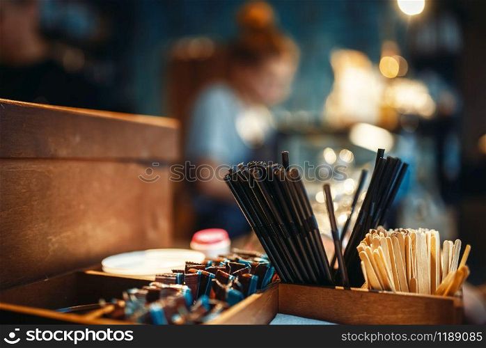 Tools for coffee drinking at bar counter closeup. Tubes, wooden sticks, sugar bags in wooden boxes, cafe interior. Tools for coffee drinking at bar counter closeup