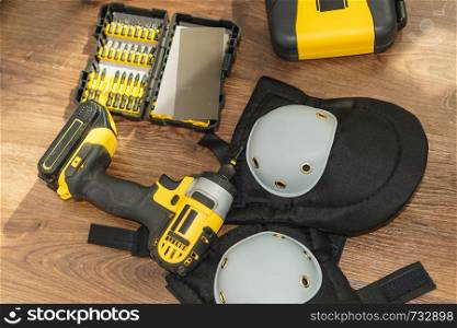 Tools for handyman renovation on wooden floor. Yellow driller tool, knee pads and drill bit set.. Drill with bit set and knee pads