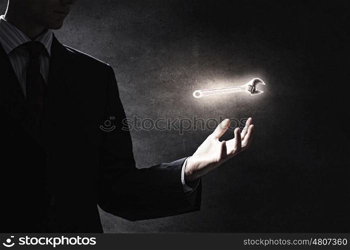 Tools for your success. Businessman on dark background holding wrench symbol in his hand