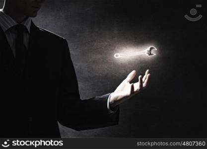 Tools for your success. Businessman on dark background holding wrench symbol in his hand