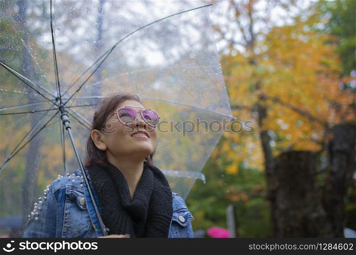toothy smiling face of woman tourist with rain umbrella standing in autumn color leaves in hokkaido japan ,hokkaido is most popular autumn season traveling destination in japan