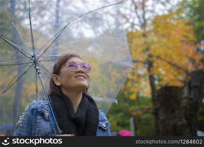 toothy smiling face of woman tourist with rain umbrella standing in autumn color leaves in hokkaido japan ,hokkaido is most popular autumn season traveling destination in japan