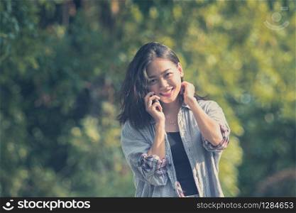 toothy smiling face of younger asian woman talking on mobile phone in green park
