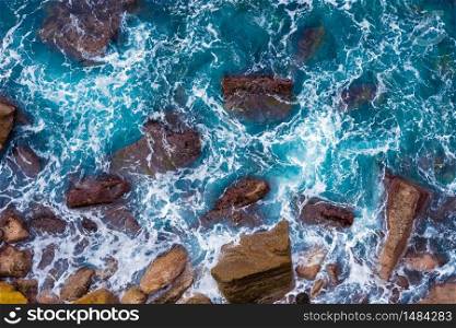 Top aerial view of blue waves crashing on rocky Australian coastline. Summer seascape with birds eye view shot over ocean waves and cliffs. Travel concept background. Top aerial view of blue waves crashing on rocky Australian coastline. Summer seascape with ocean waves and cliffs. Travel concept background