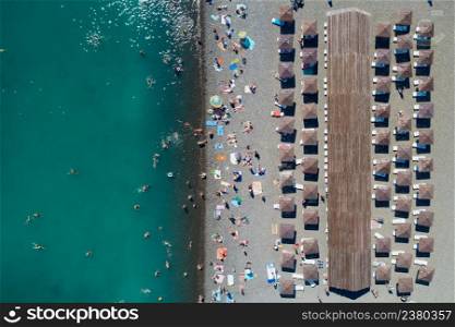 Top aerial view of the pebble beach. Rows of umbrellas and sunbeds, warm blue sea and holiday makers having fun. Copy space
