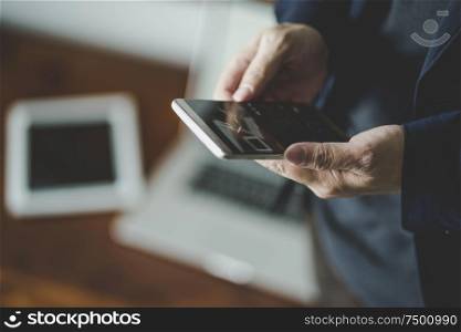 Top angle and closeup view of businessman using the smartphone with blur laptop and digital pad background .