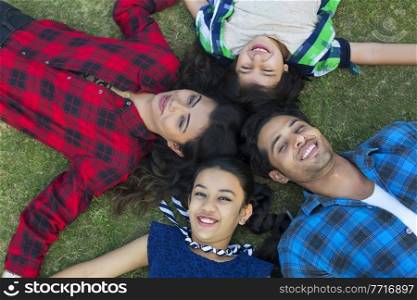 Top angle view of a happy family of man woman son and daughter lying down in park in four directions looking up.