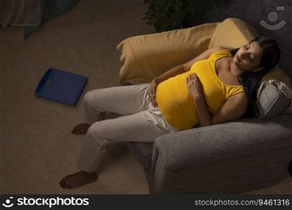 Top angle view of a pregnant woman relaxing on sofa at home