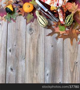 Top border of autumn dinner setting with real gourd decorations, leaves and acorns on top of rustic wood