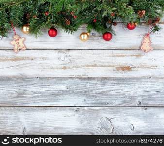 Top border of Christmas evergreen branches with other holiday decorations on white rustic wood