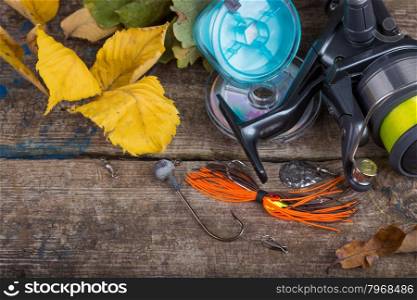 top fishing tackles reel, line and lure on wooden board with leafs of autumn