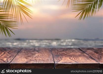 Top of wood table on blurred sea on the sunset with coconut tree background . Empty ready for your product display montage. Concept of beach in summer.. Empty wooden table and palm leafs on a background of beach blurred.