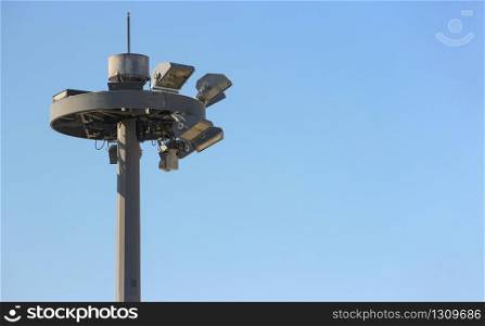 Top part of tall and high airport light pole with clear sky as background.