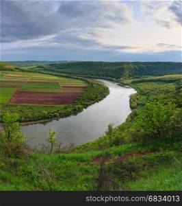 Top picturesque evening view of spring fields on Dnister river bend canyon. Unrecognizable rafting tourist camp far below on riverside. Ternopil region, Ukraine, Europe. Three shots stitch panorama.