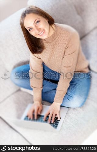 Top shot of caucasian smiling woman working with computer on the sofa