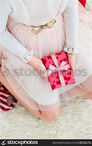Top shot of girl wearing dress holding Christmas gift and sitting on a carpet