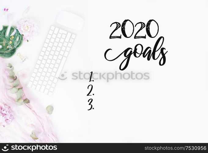 Top view 2020 goals list with modern silver keyboard with female accessories and peony flowers, copy space on white background. Top view home office workspace