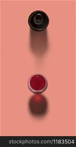 Top view above opened bottle and glass of red wine on a pastel coral background with soft dark shadows, copy space. Red wine in a glass with opened bottle with shadows.