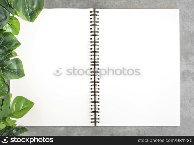Top view and flat lay with blank sketchbook and green leaves over cement background. blank sketchbook and green leaves
