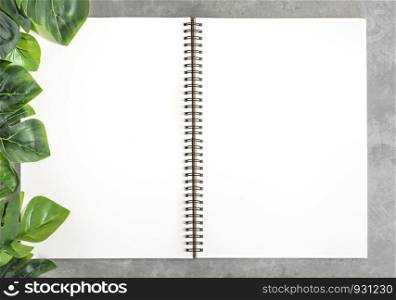 Top view and flat lay with blank sketchbook and green leaves over cement background. blank sketchbook and green leaves