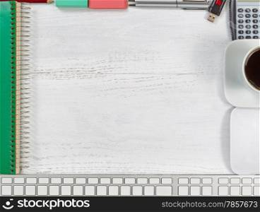 Top view angle of a white wooden desktop with border of business office objects consisting of computer, mouse, pencil, pen, eraser, spiral notepad, coffee, calculator and thumb drive.