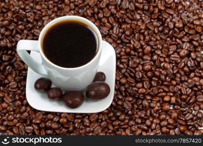 Top view angle of freshly made dark coffee, with chocolate on platter, resting in a sea of roasted coffee beans.