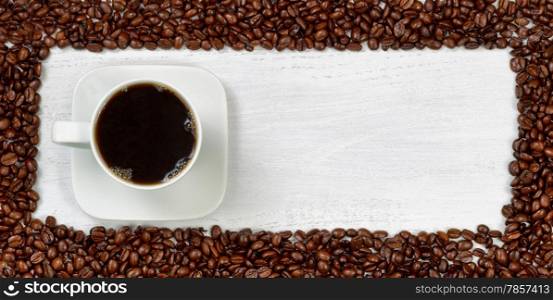 Top view angle of freshly made dark coffee with roasted coffee beans, forming even border, on white wooden table.