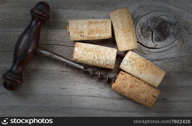 Top view angled shot of antique corkscrew with five used corks on rustic wood. Special lighting and vignette border added to image to enhance vintage appearance.