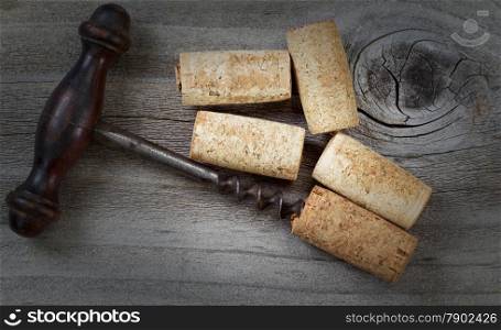 Top view angled shot of antique corkscrew with five used corks on rustic wood. Special lighting and vignette border added to image to enhance vintage appearance.